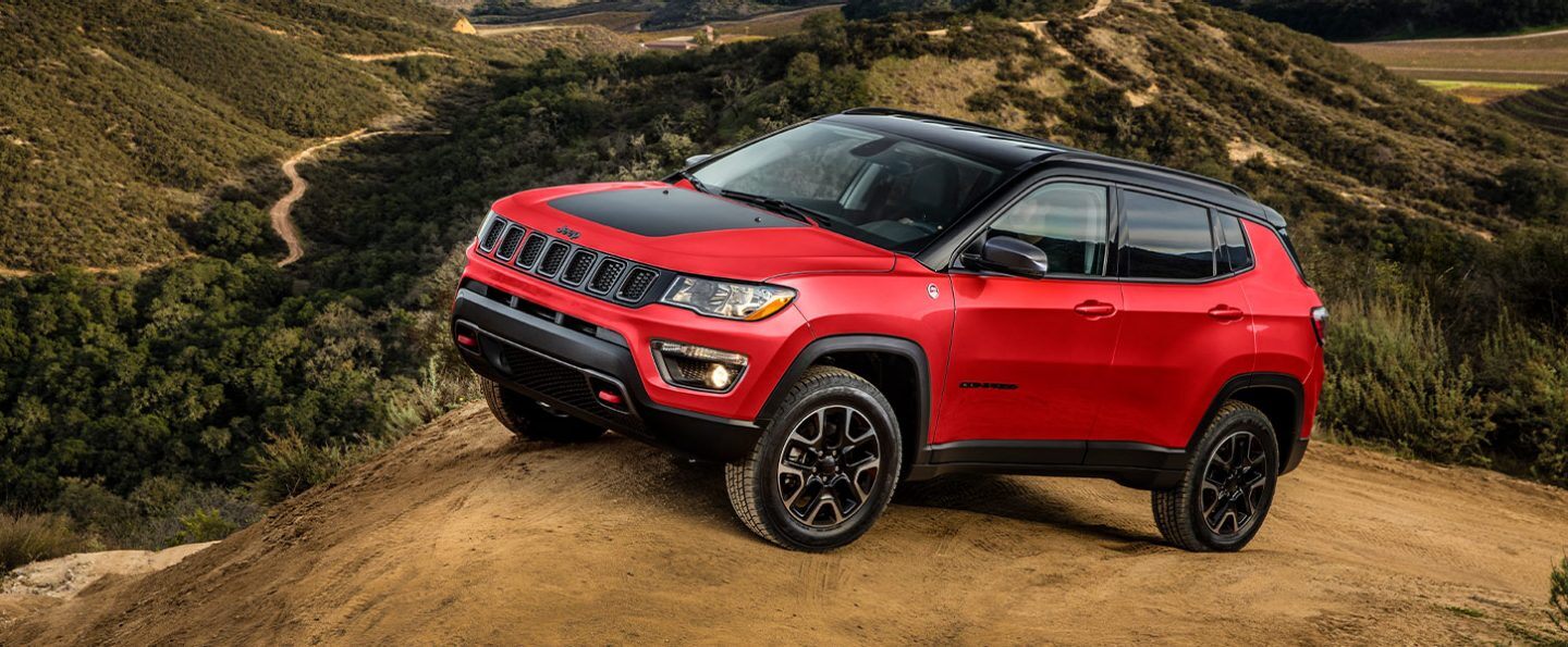A red 2021 Jeep Compass Trailhawk parked on a hilltop in a mountain range.