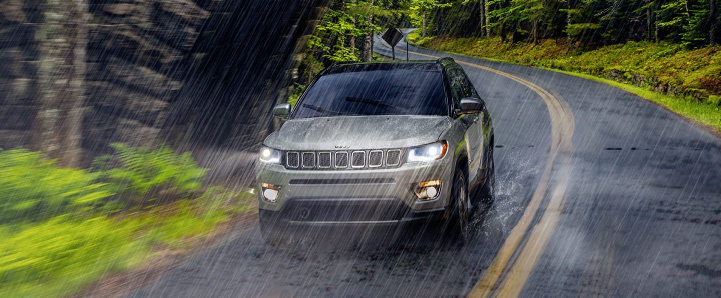 The 2021 Jeep Compass being driven in heavy rain on a winding road.