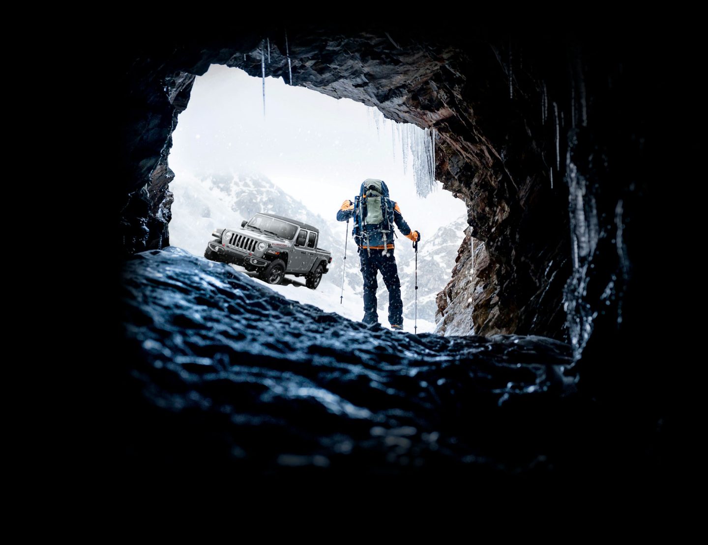 The 2022 Jeep Gladiator Rubicon as a mountain climber walks toward it, emerging from a frigid cavern in the snow-covered mountains.